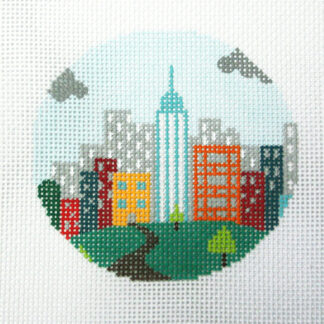 Circular embroidery depicting a city skyline with a tall central tower, colorful buildings, and a green park with a winding path.