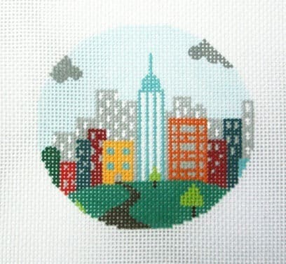 Circular embroidery depicting a city skyline with a tall central tower, colorful buildings, and a green park with a winding path.