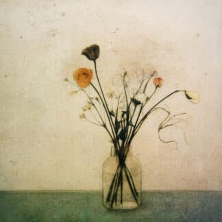 Glass vase with tall dried stems and orange poppies arranged on a pale blue-green surface in a simple still-life composition.