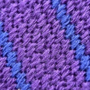 Close-up of purple knitted fabric with a blue stripe pattern showing textured stitches.