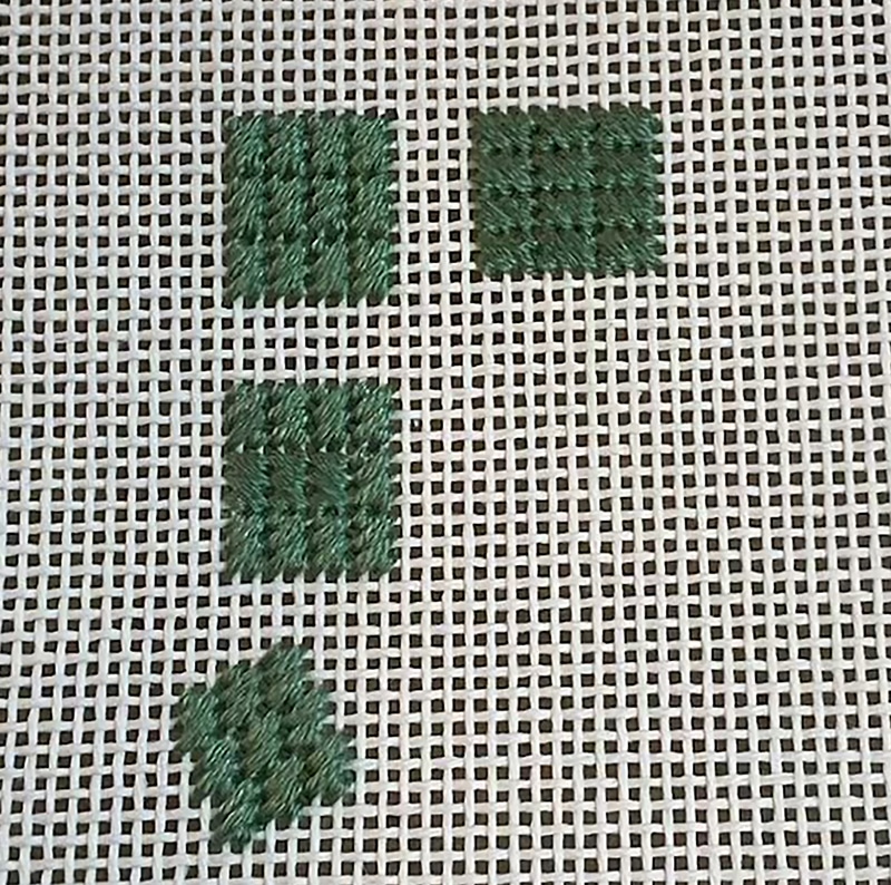 Cross-stitched dark green squares on open-weave fabric, arranged in a loose L-shape: two squares in the top row (left and right) and two more squares below on the left.
