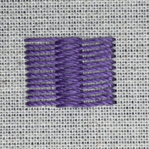 Close-up of a square patch of purple embroidery stitches on light fabric with visible weave